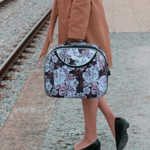 Stylish woman in a coat poses with luggage on a railway track, showcasing travel fashion.