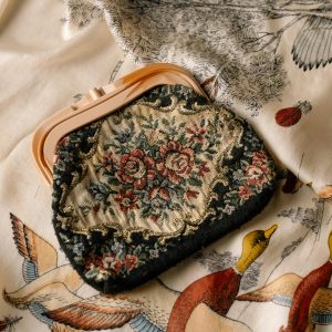 A vintage floral clutch bag resting on a patterned fabric with bird illustrations.